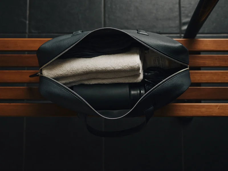 Otwarta torba sportowa pakowana ręcznikiem, butelką i rękawicami na ławce w szatni